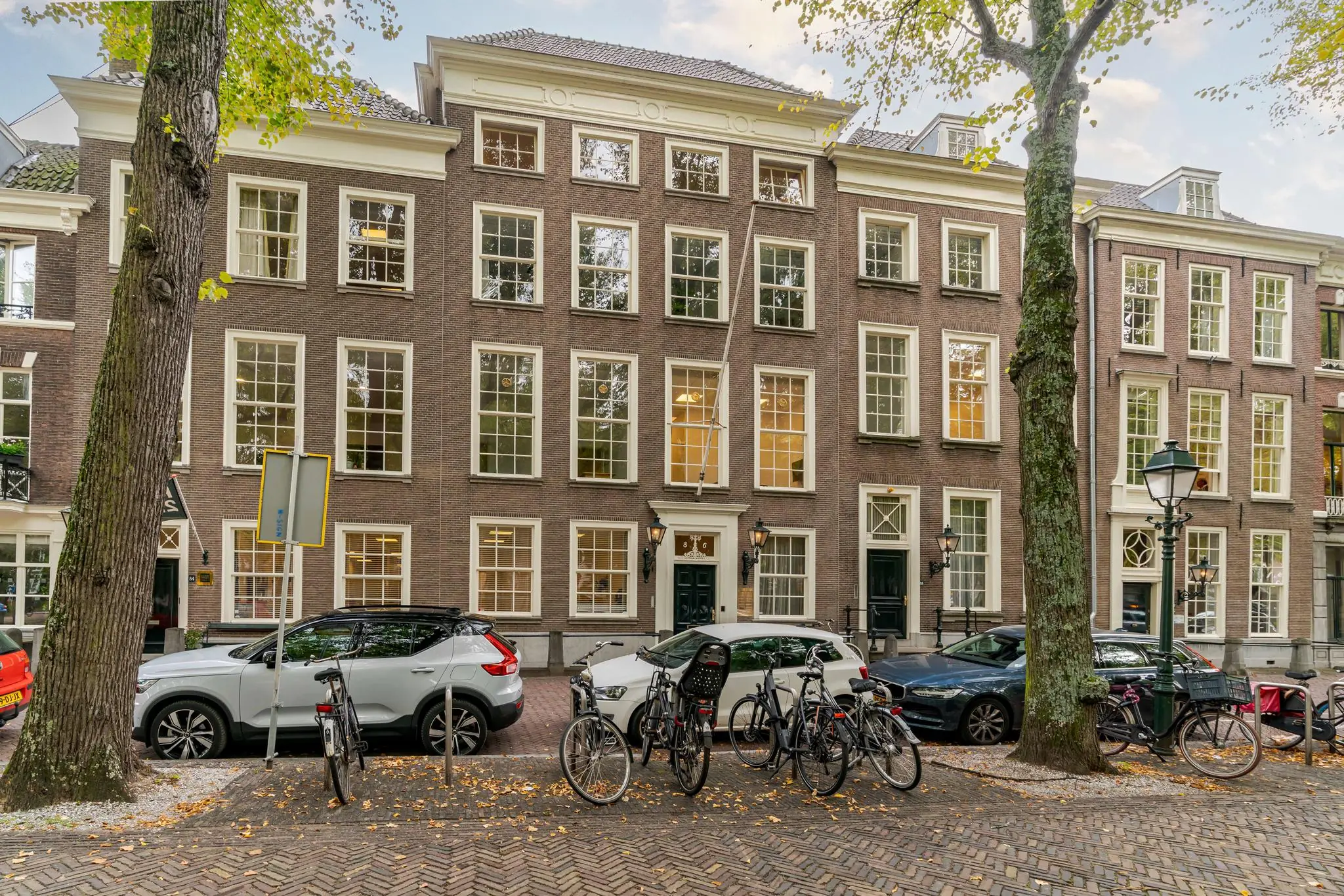 Gevels van statige herenhuizen aan het Lange Voorhout in Den Haag met geparkeerde auto's en fietsen op de voorgrond.